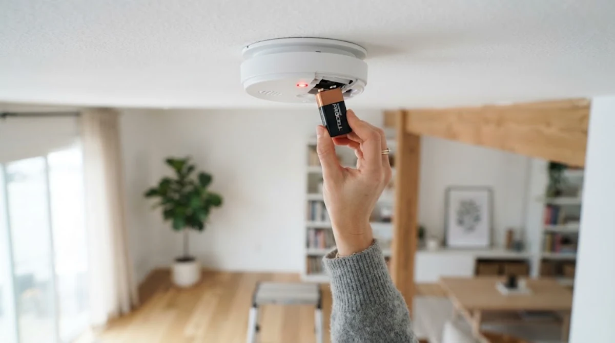 Hand replacing the battery in a beeping smoke detector on a living room ceiling